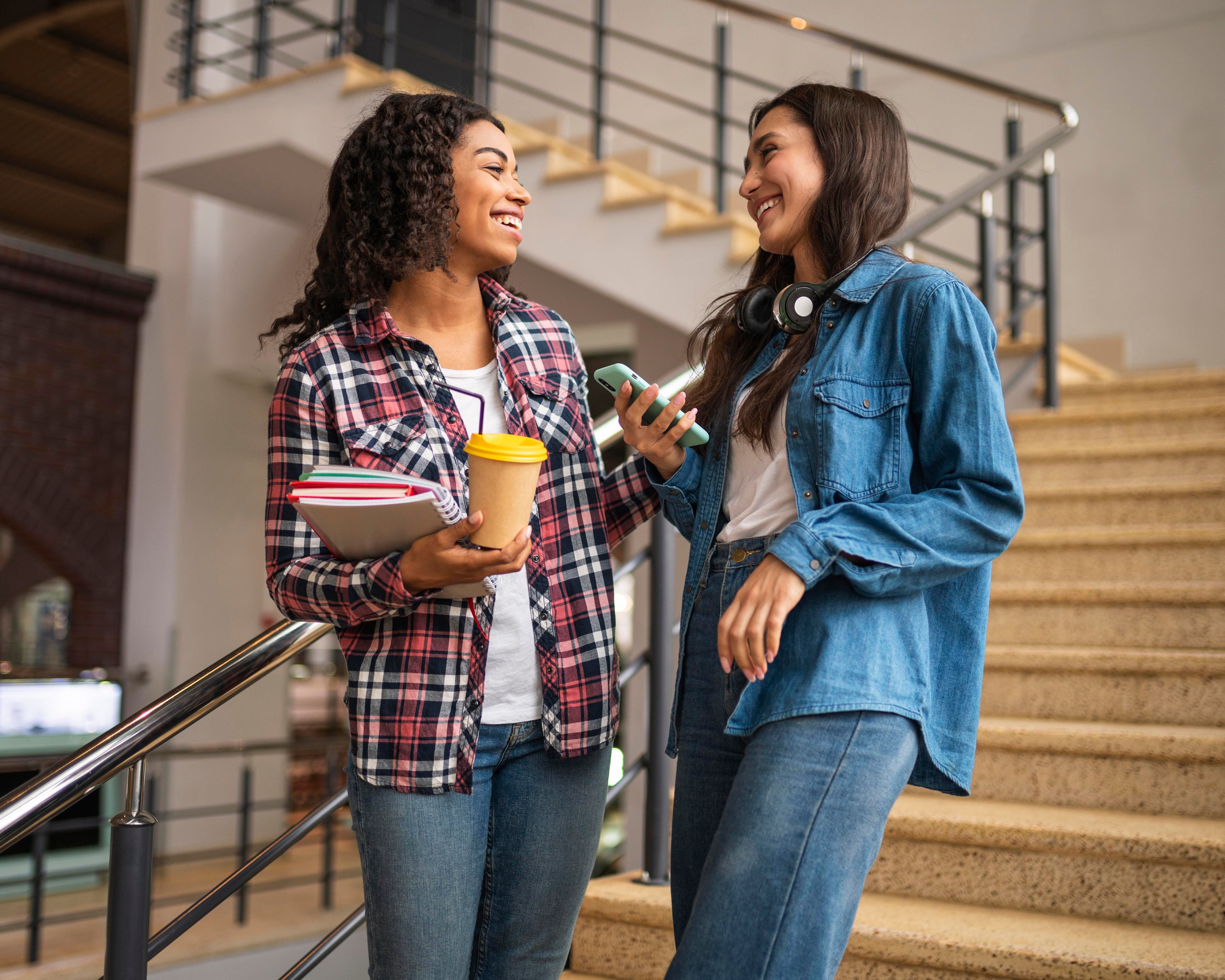 Two female friends talking on the staircase in a university building.